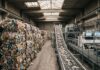 Beyond Handouts: Why Plastic Recyclers Must Reinvent Their Business Model to Survive Balle di rifiuti in plastica stoccate all'interno di un impianto industriale di riciclo con macchinari di selezione sullo sfondo