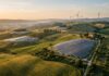 Campi coltivati e impianti di energia solare ed eolica integrati nel paesaggio collinare italiano illuminati dalla luce calda dell'alba.